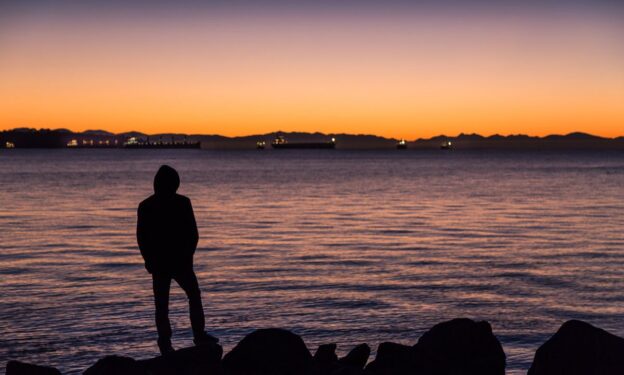 A photo of a man standing by the ocean looking out onto the horizon, concept of overcoming opiate addiction.