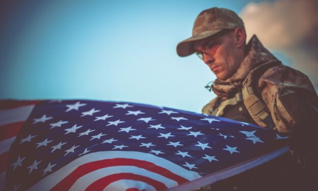 Young Army Veteran with American Flag Closeup Photo. Army Trooper with USA Flag. Concept of veterans and addiction.